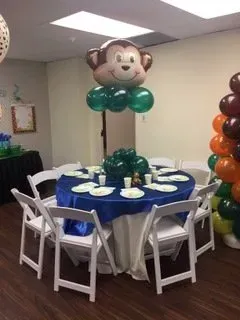 A table with plates and chairs and a monkey balloon on top of it.
