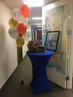 A blue table with balloons and a picture on it in a hallway.