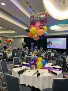 A room filled with tables and chairs decorated with balloons for a party.