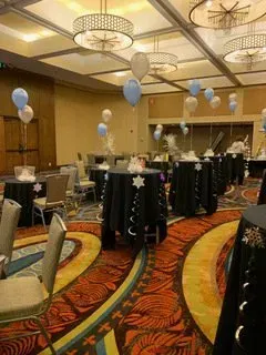 A large room with tables and chairs and balloons hanging from the ceiling.