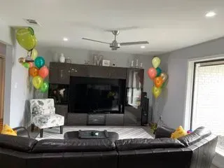 A living room with a couch , chair , television and balloons.