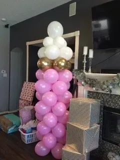 A bunch of pink and white balloons are stacked on top of each other in a living room.