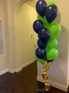 A bunch of blue and green balloons are sitting on a wooden floor in a room.