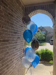 A bunch of blue and white balloons are sitting in front of a brick wall.