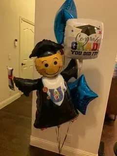 A balloon in the shape of a graduation cap and gown is holding a diploma.