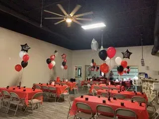 A room filled with tables and chairs decorated with red , white and black balloons.
