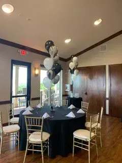 A room with tables and chairs and balloons on the tables.