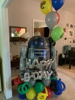 A r2d2 balloon is surrounded by balloons in a living room.