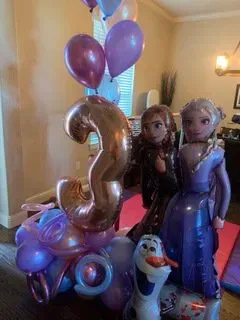 A bunch of balloons with anna and elsa on them are in a room.