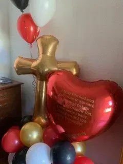 A red heart balloon is sitting next to a gold cross balloon.