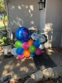 A bunch of colorful balloons are sitting on the sidewalk in front of a house.
