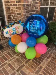 A bunch of balloons are sitting on a brick sidewalk in front of a brick building.