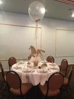 A round table with a horse centerpiece and a balloon hanging from the ceiling.