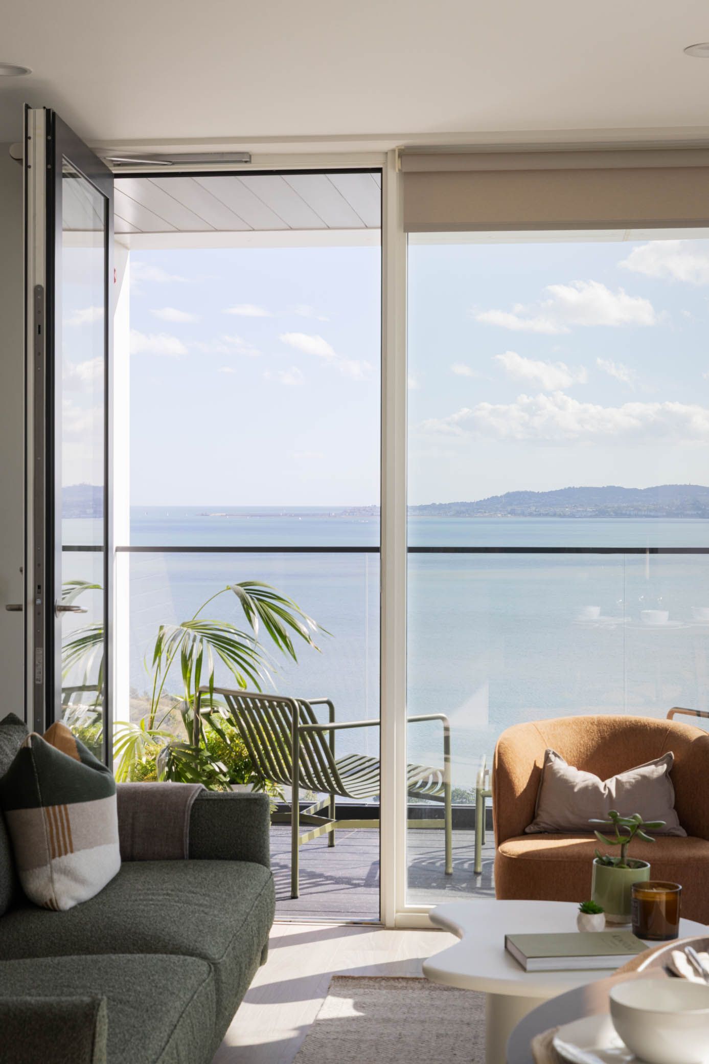 Bright living room opening to a balcony with sea view, wicker chairs, sofa, and coffee table