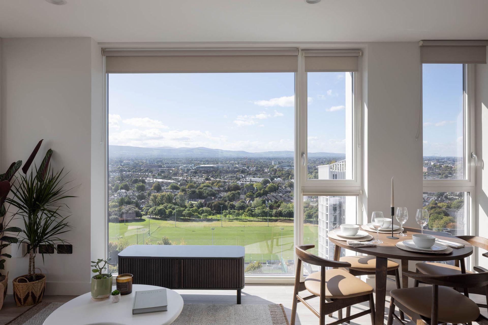 Bright apartment dining area with a large window overlooking a city and green park.