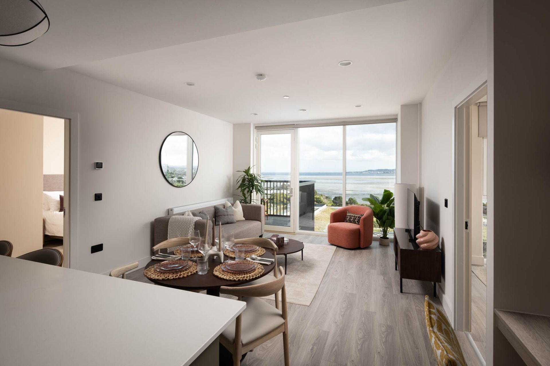 Bright modern dining and living room with table set, sofa, and balcony view of water.