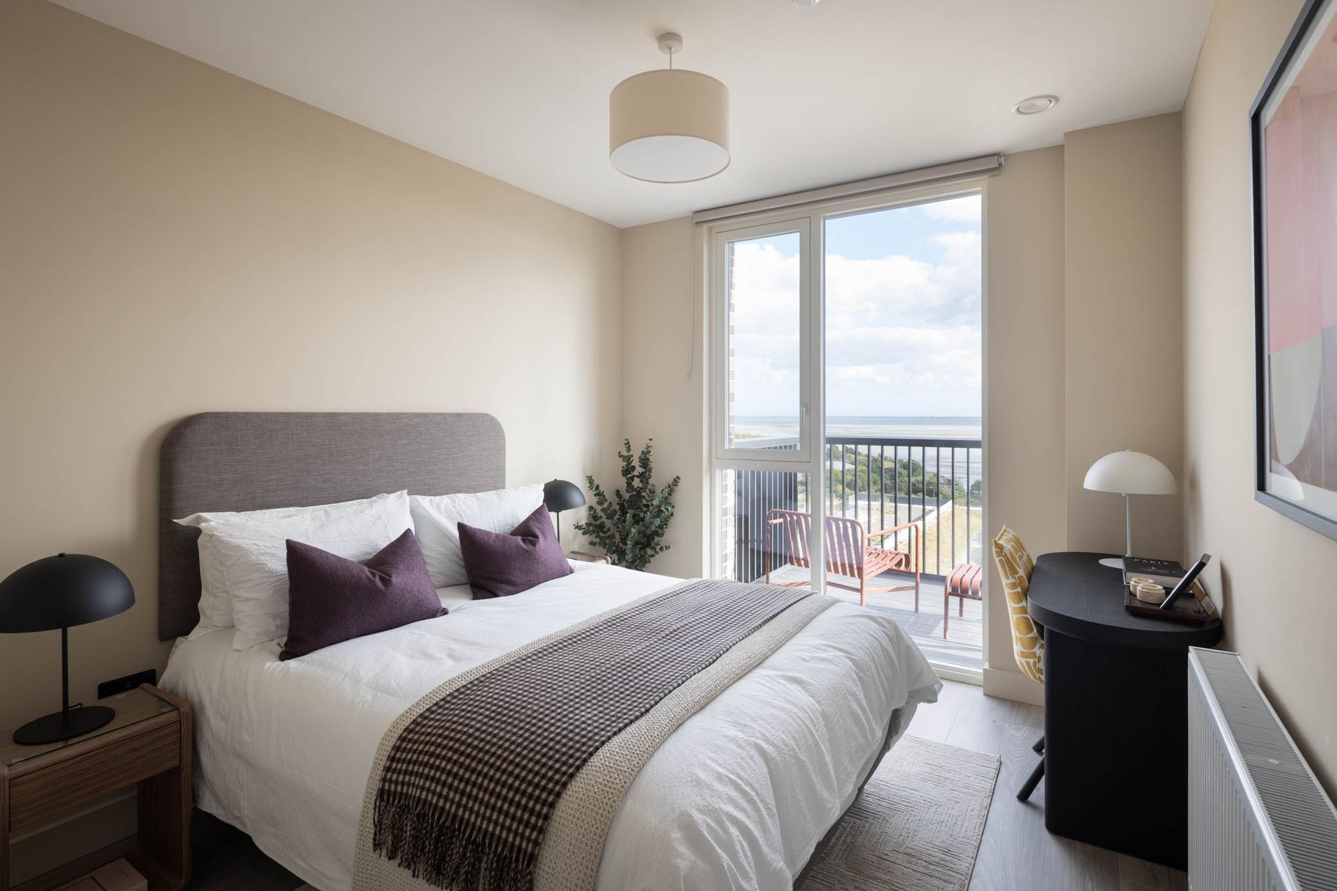 Bright bedroom with gray bed, purple pillows, and balcony doors overlooking a view.