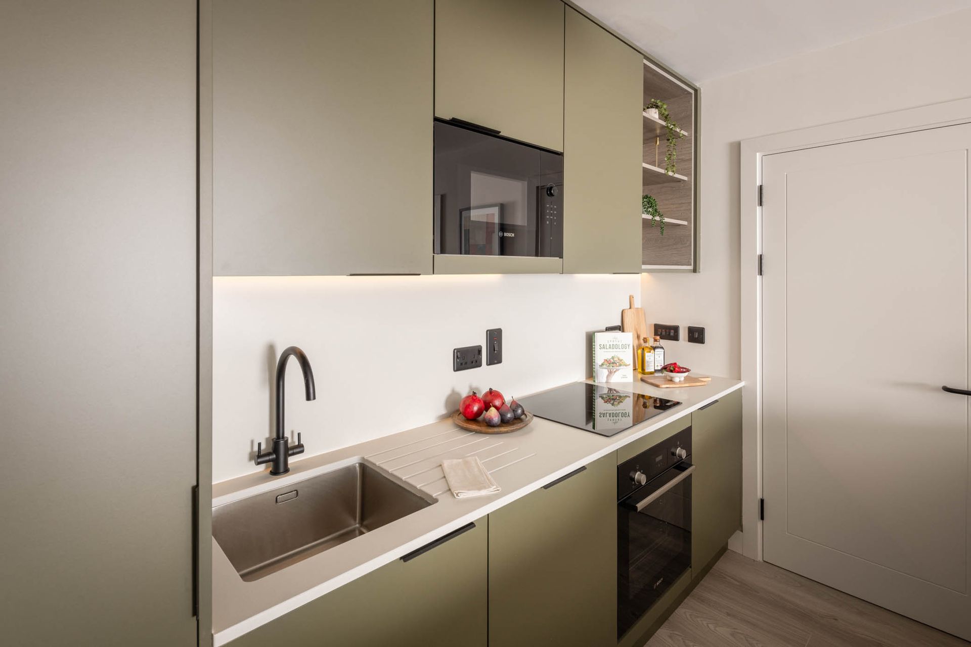 Modern beige kitchen with sink, built-in oven, countertop appliances, and white door.