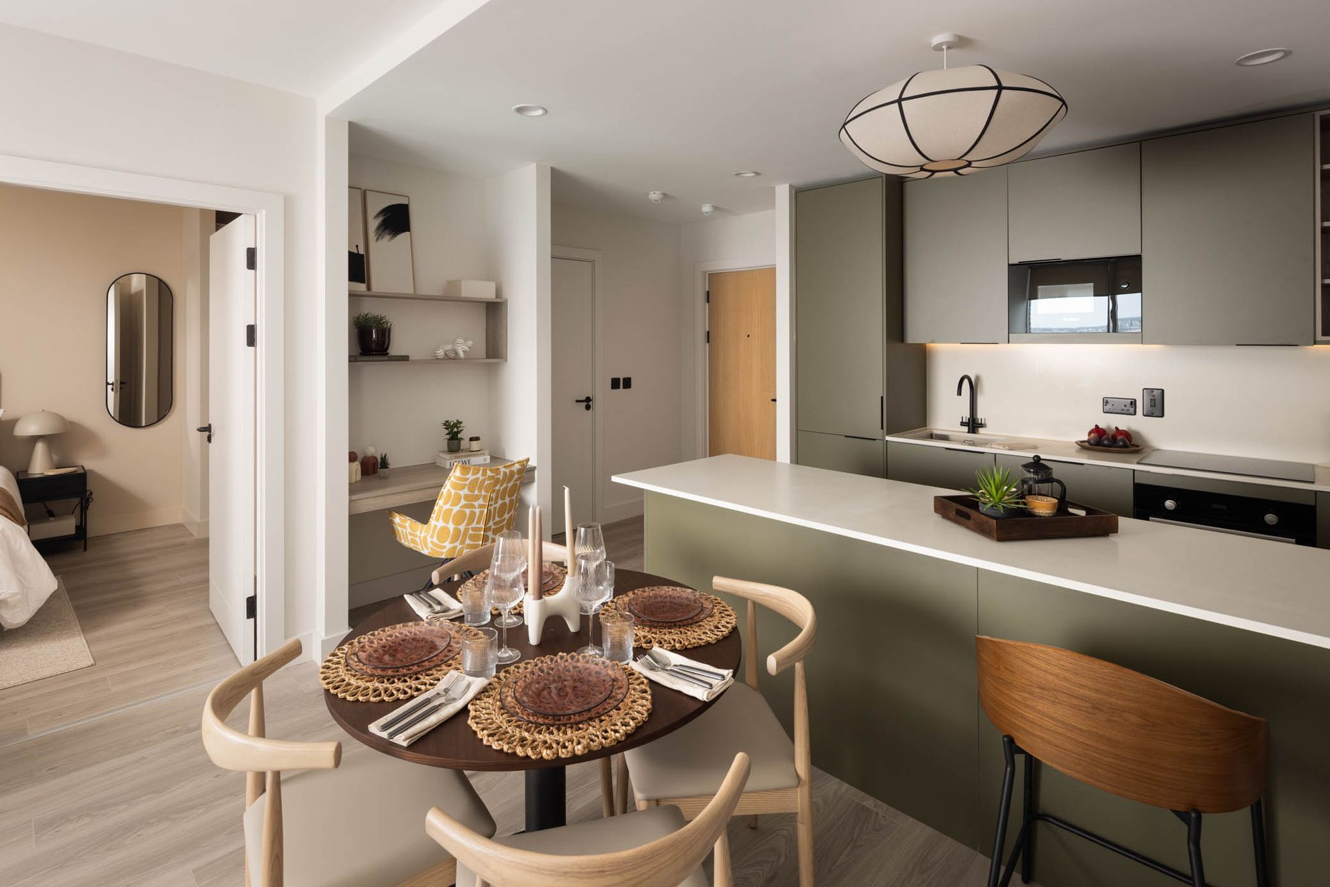 Modern open-plan kitchen and dining area with neutral decor, curved island, and set table near the entrance.
