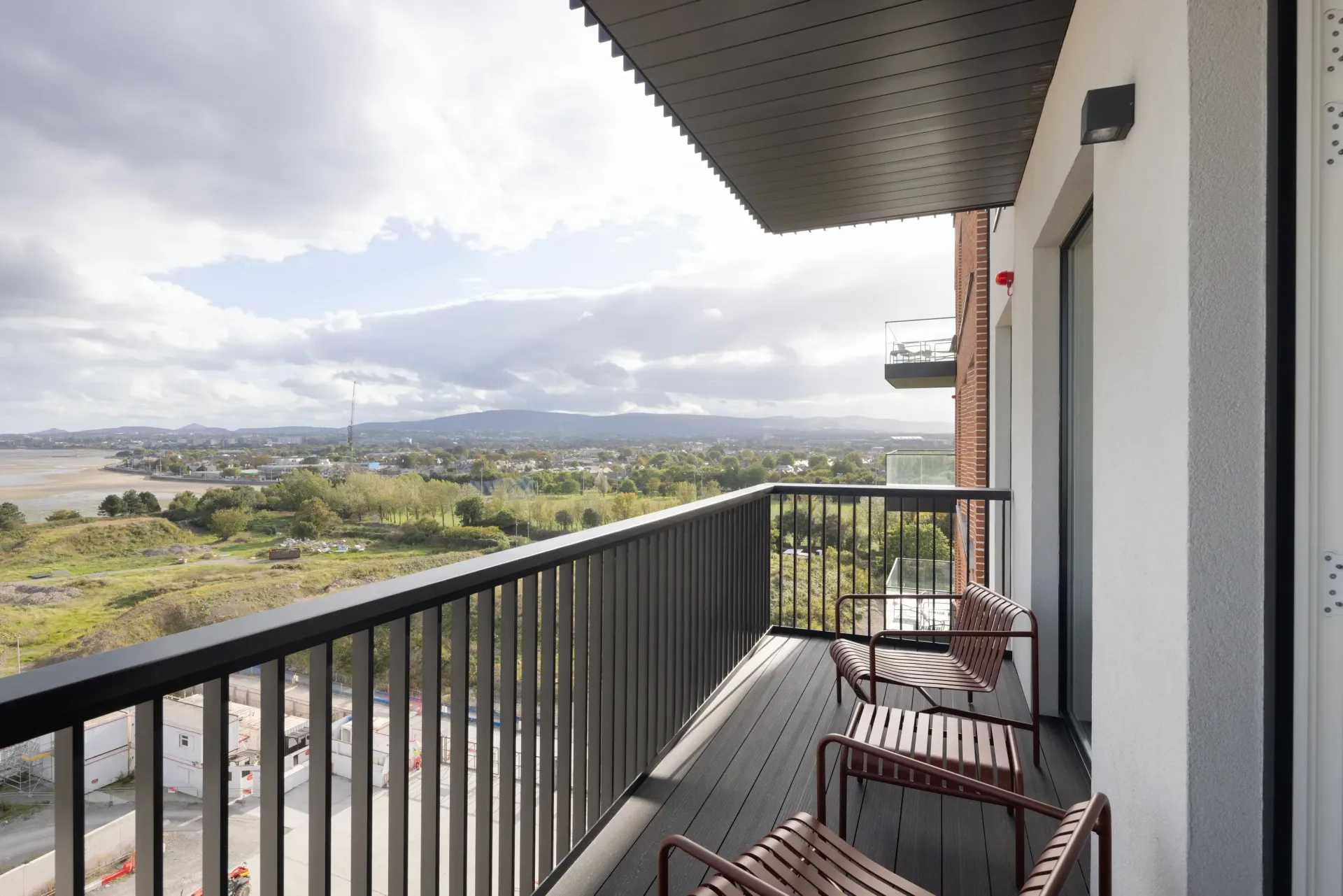 Balcony with black railing and chairs overlooking a cloudy landscape and distant hills