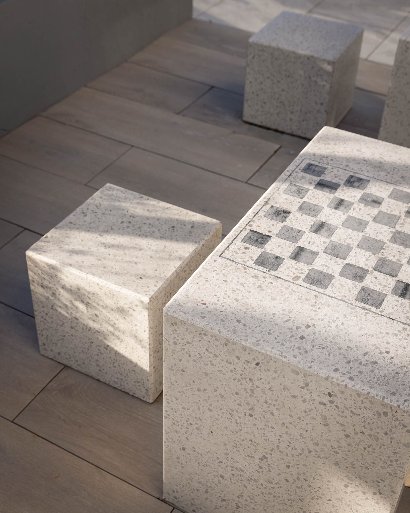 Sunlit stone cubes arranged on a tiled floor, one with a checkered top surface