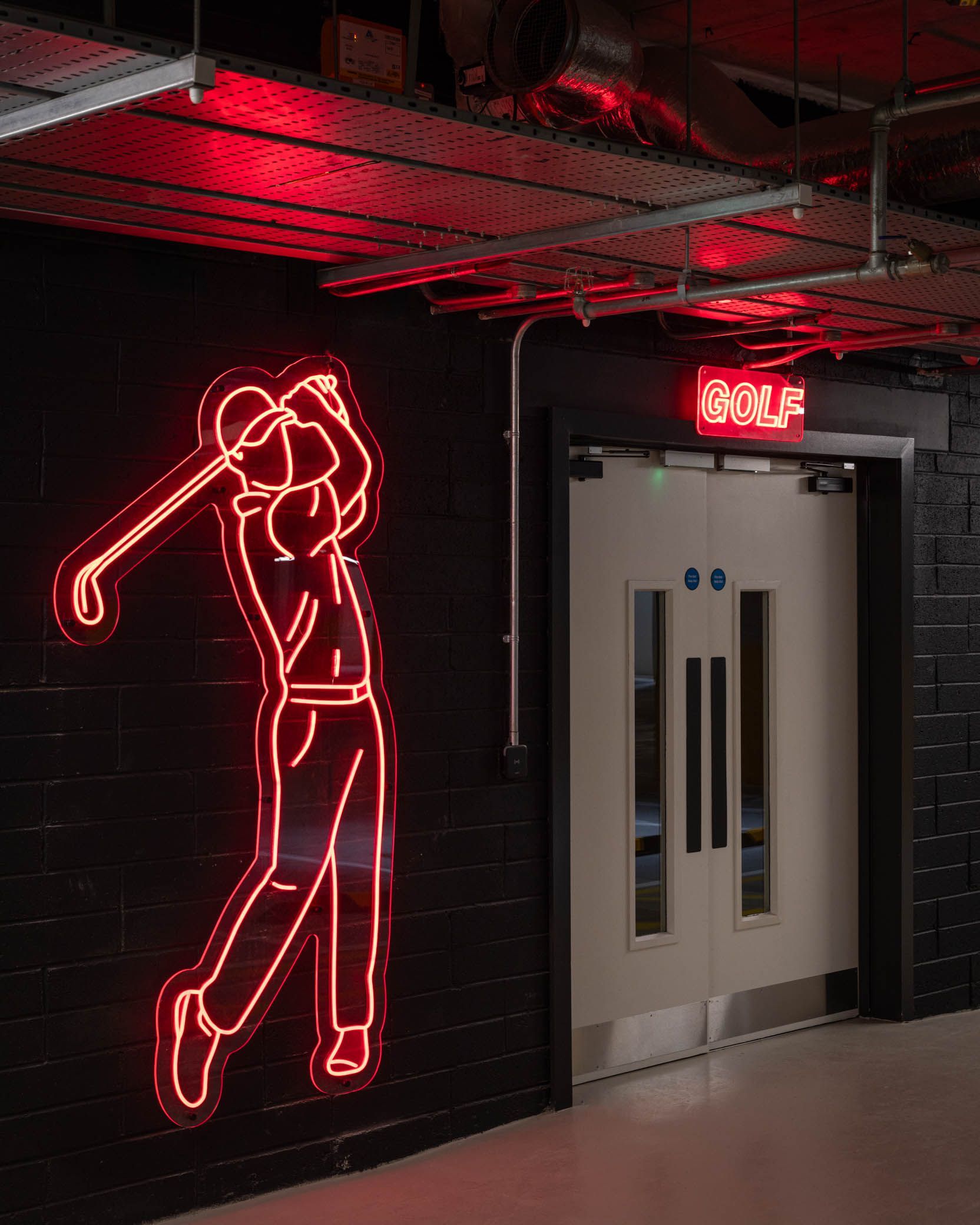 Neon red golfer sign beside a doorway in a dark hallway with a red-lit ceiling