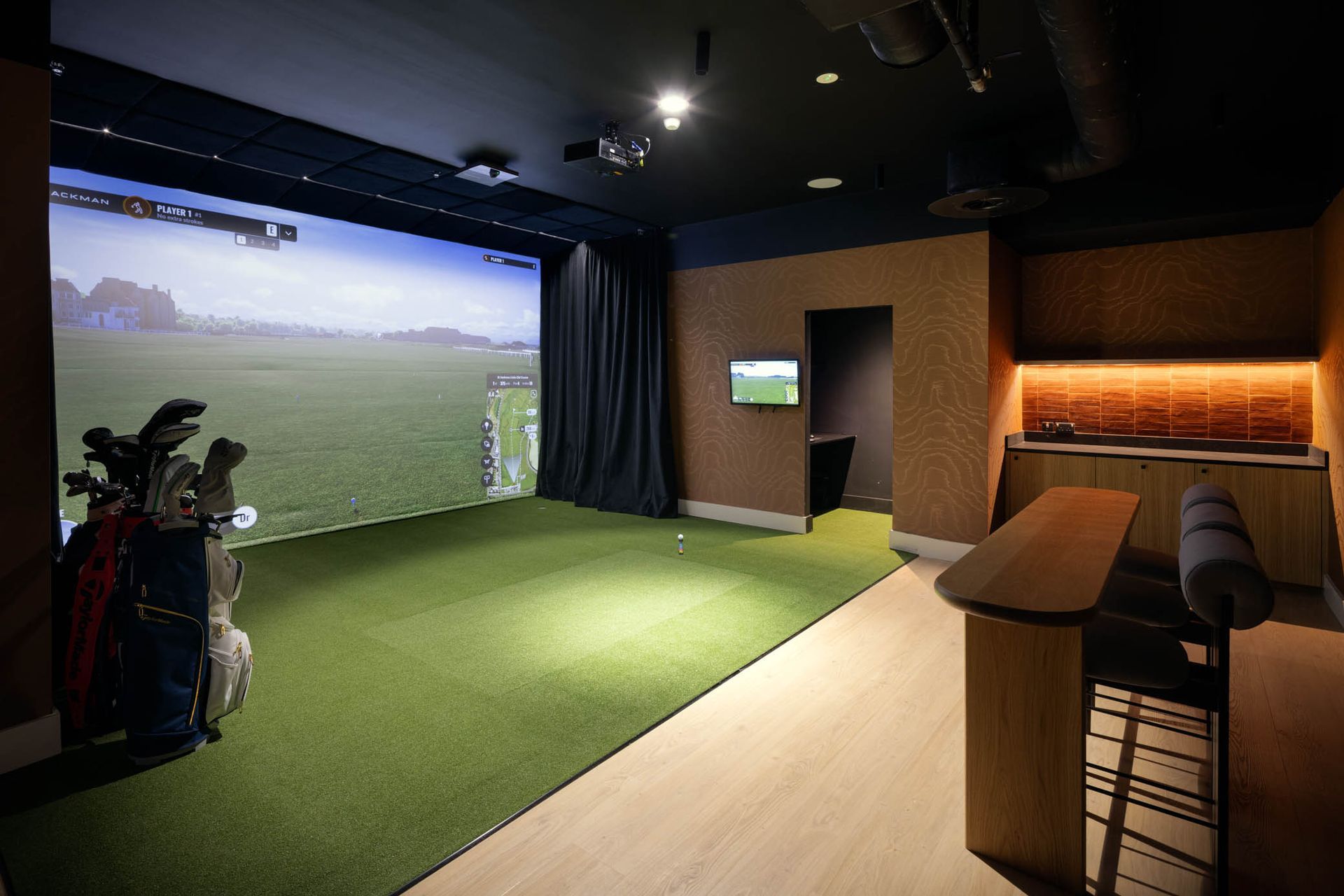 Indoor golf simulator room with large projection screen, putting green, and seating area
