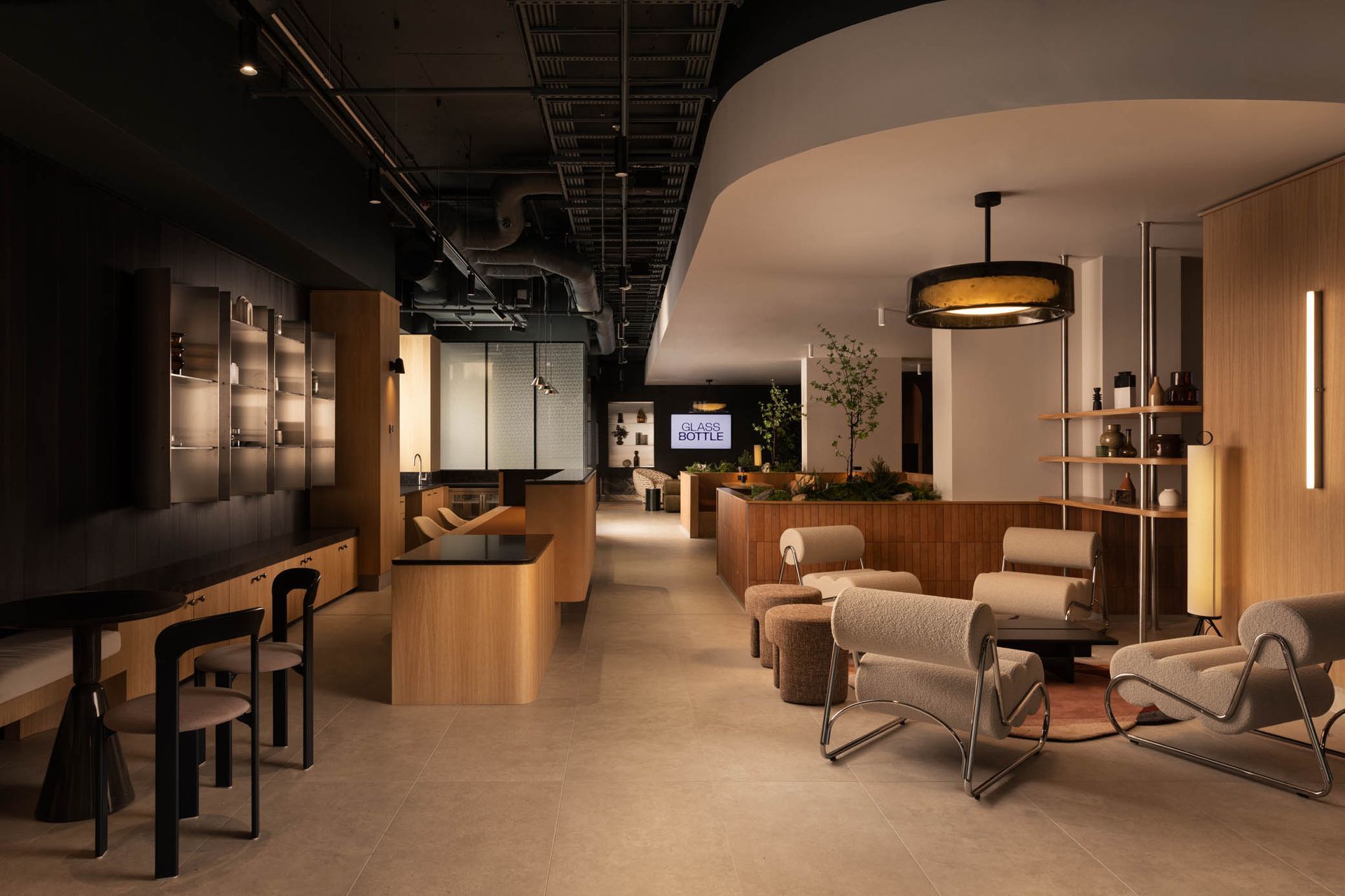 Modern lounge with warm lighting, bar stools, sofas, and wood accents in an open office or hotel lobby