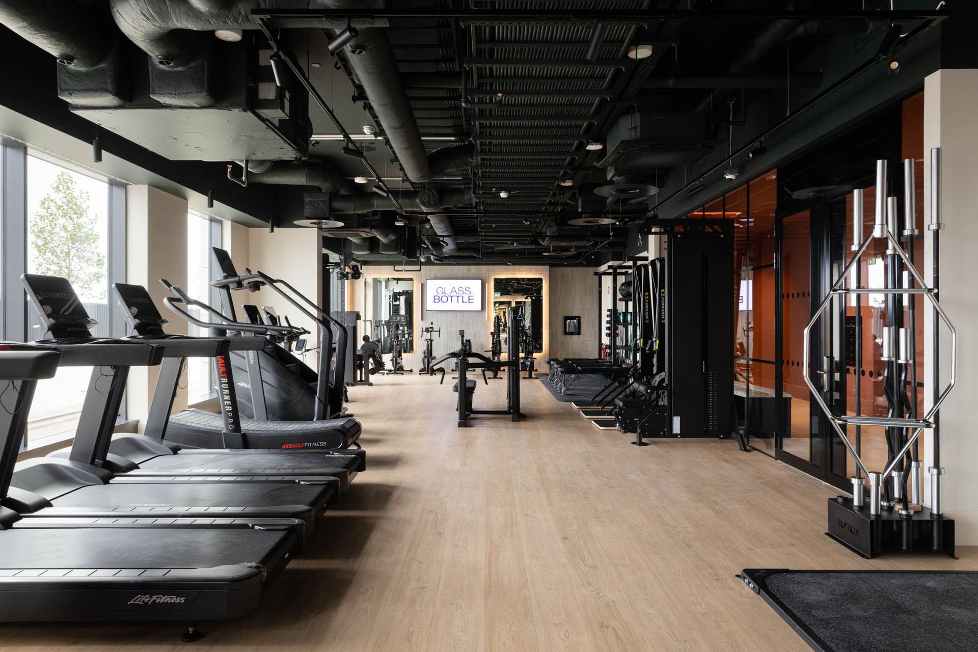 Modern gym interior with treadmills, weight machines, and wood flooring