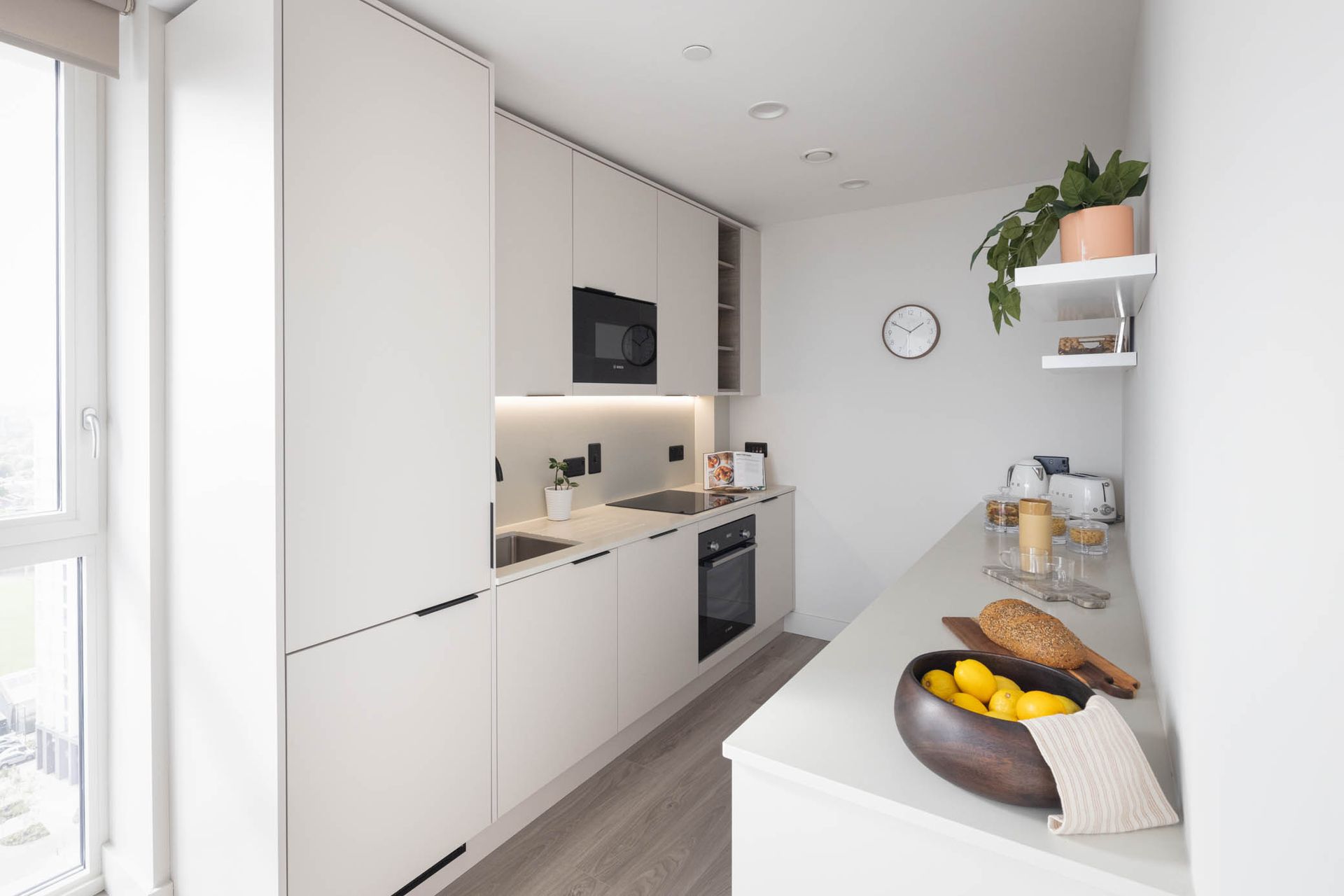 Bright modern galley kitchen with white cabinets, built-in appliances, and a fruit bowl on the counter.