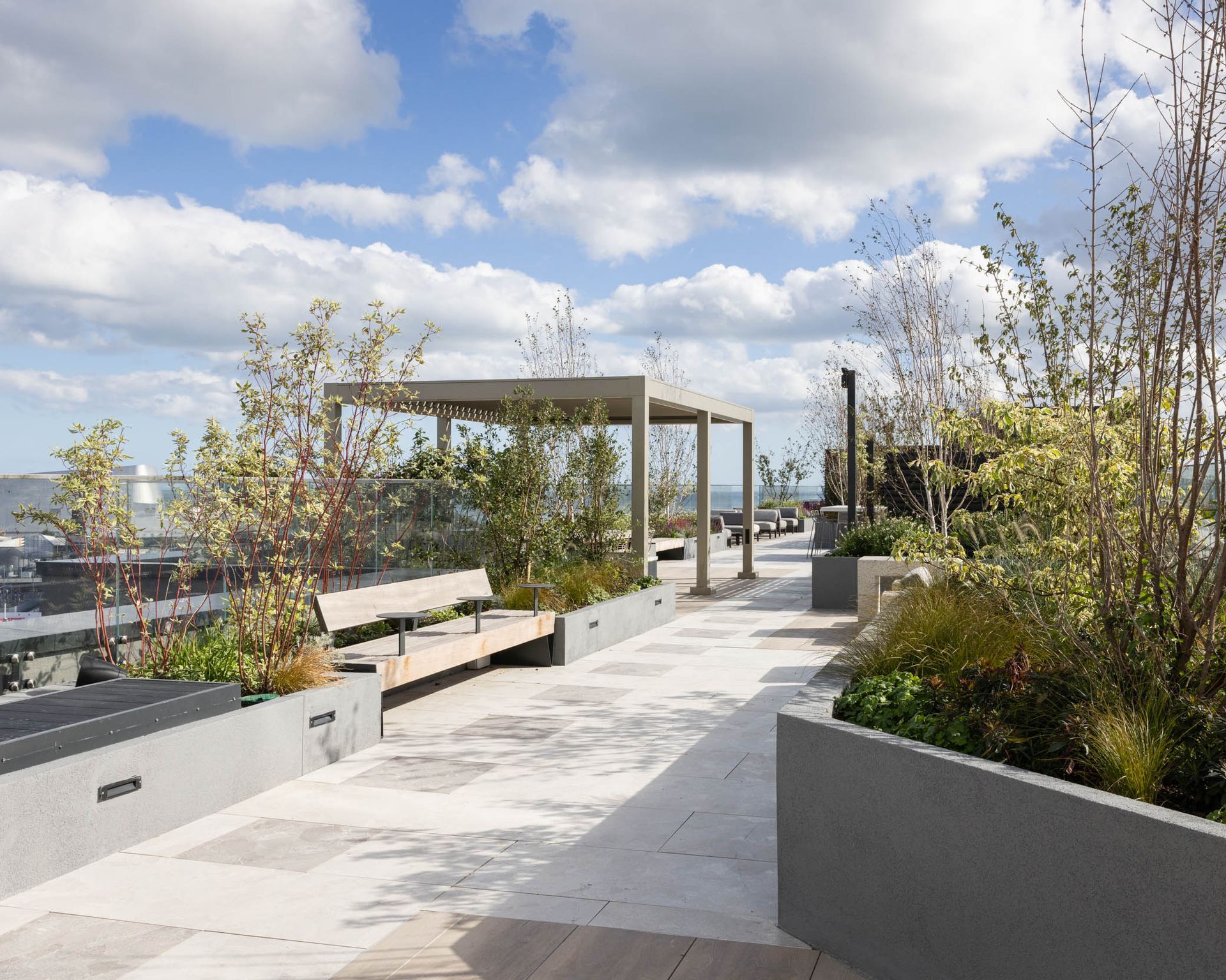 Rooftop garden terrace with benches, planters, and a pergola under a cloudy sky