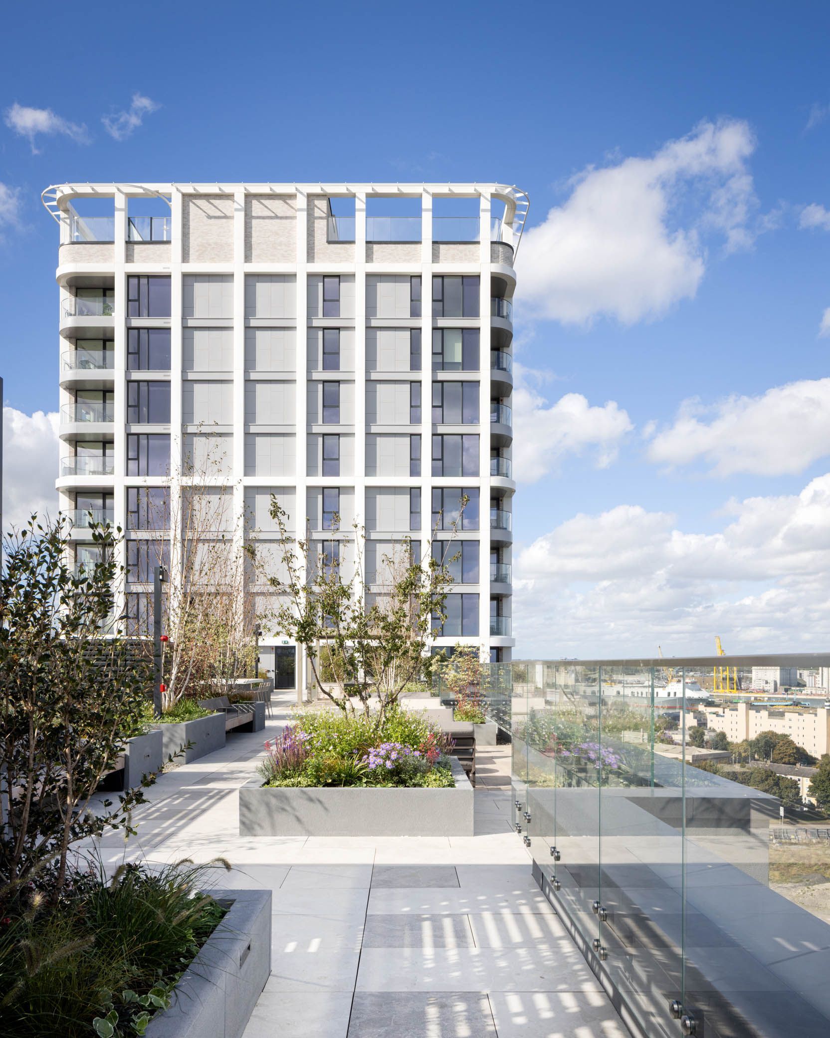 Modern white apartment building with rooftop terrace and city view under a blue sky