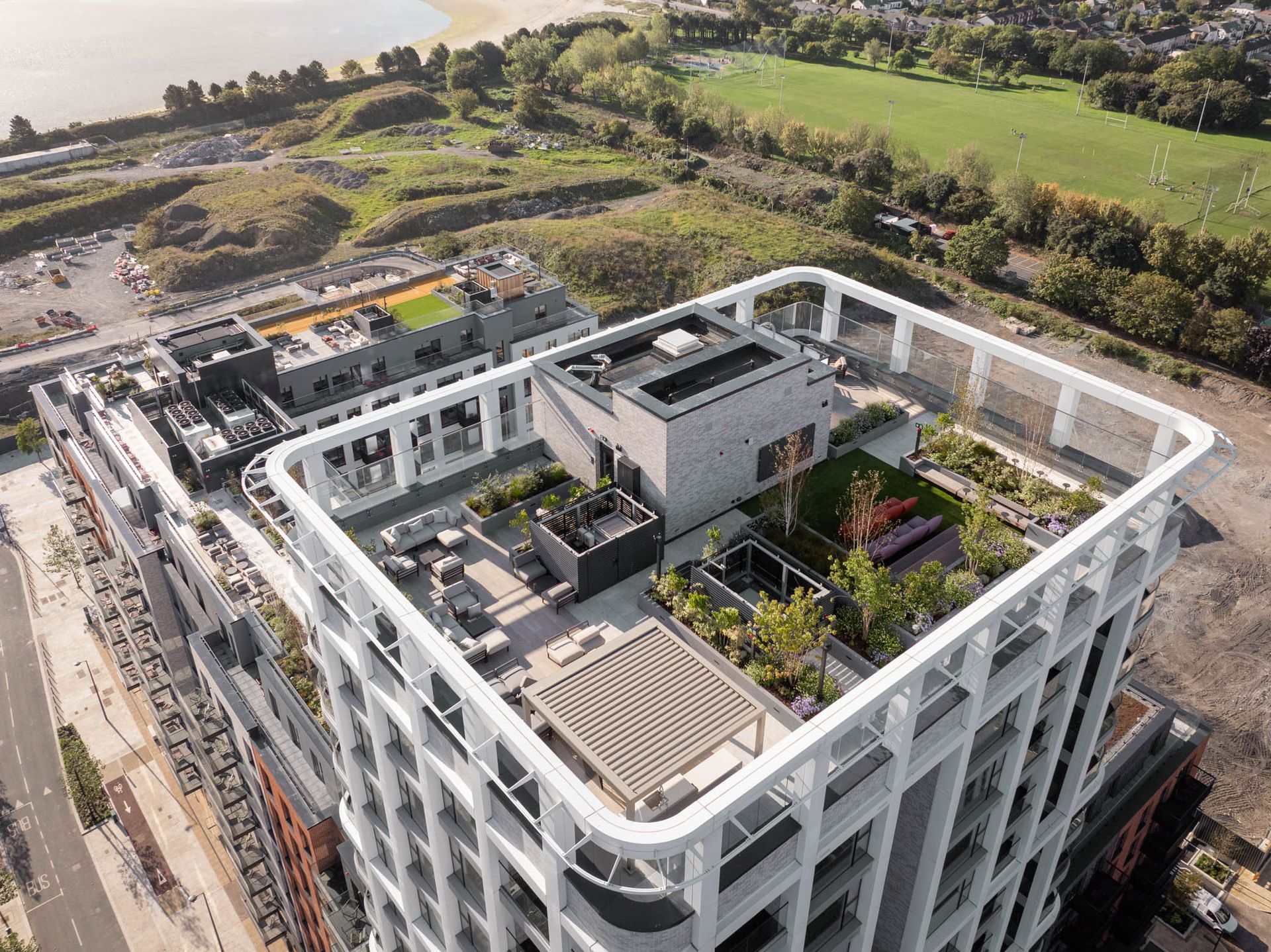Aerial view of a modern apartment building with rooftop terraces beside open green fields.