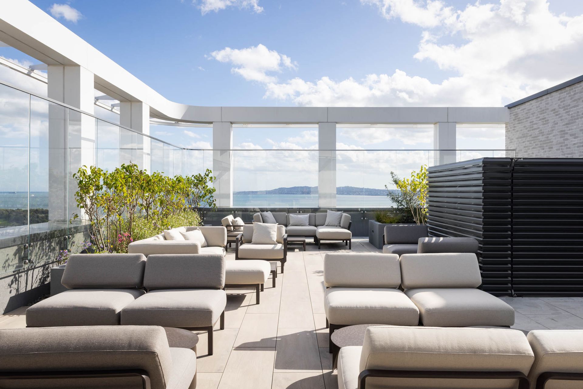 Modern rooftop lounge with gray sectional seating, white pergola, and ocean view