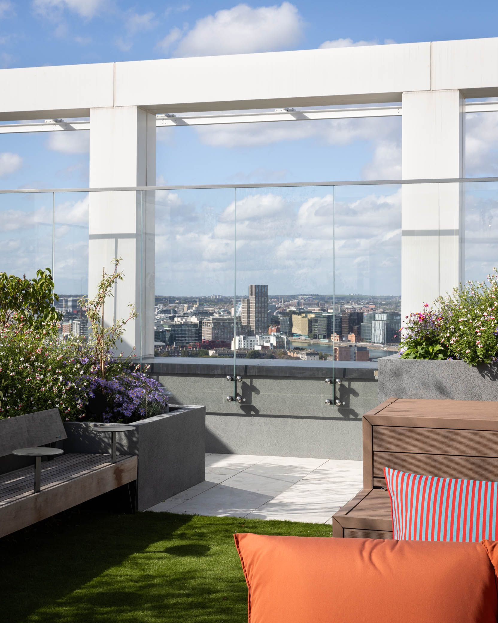 Rooftop terrace with lounge seating and a city skyline view under a blue sky.