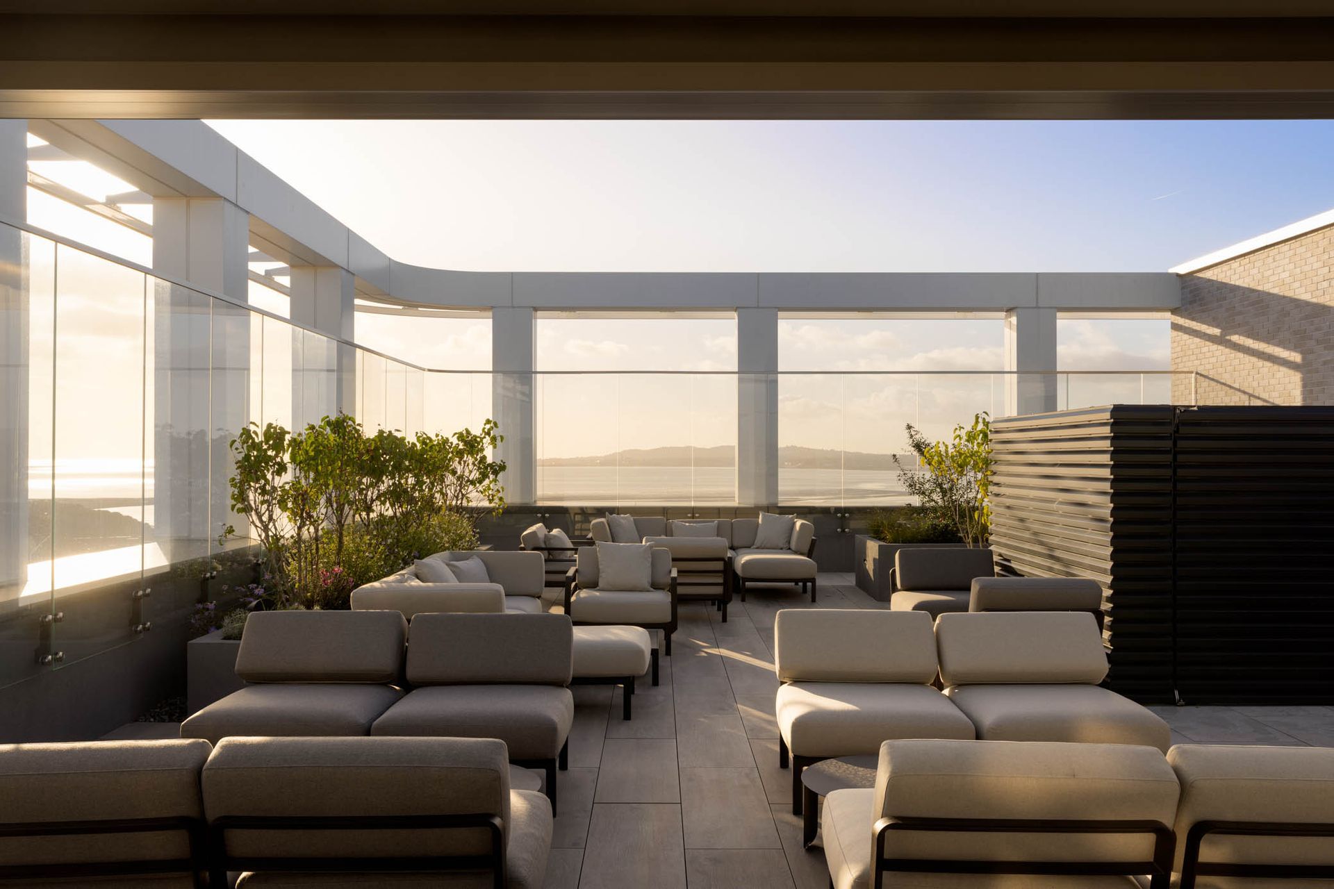 Rooftop terrace with gray lounge chairs, tables, and potted plants in warm sunlight