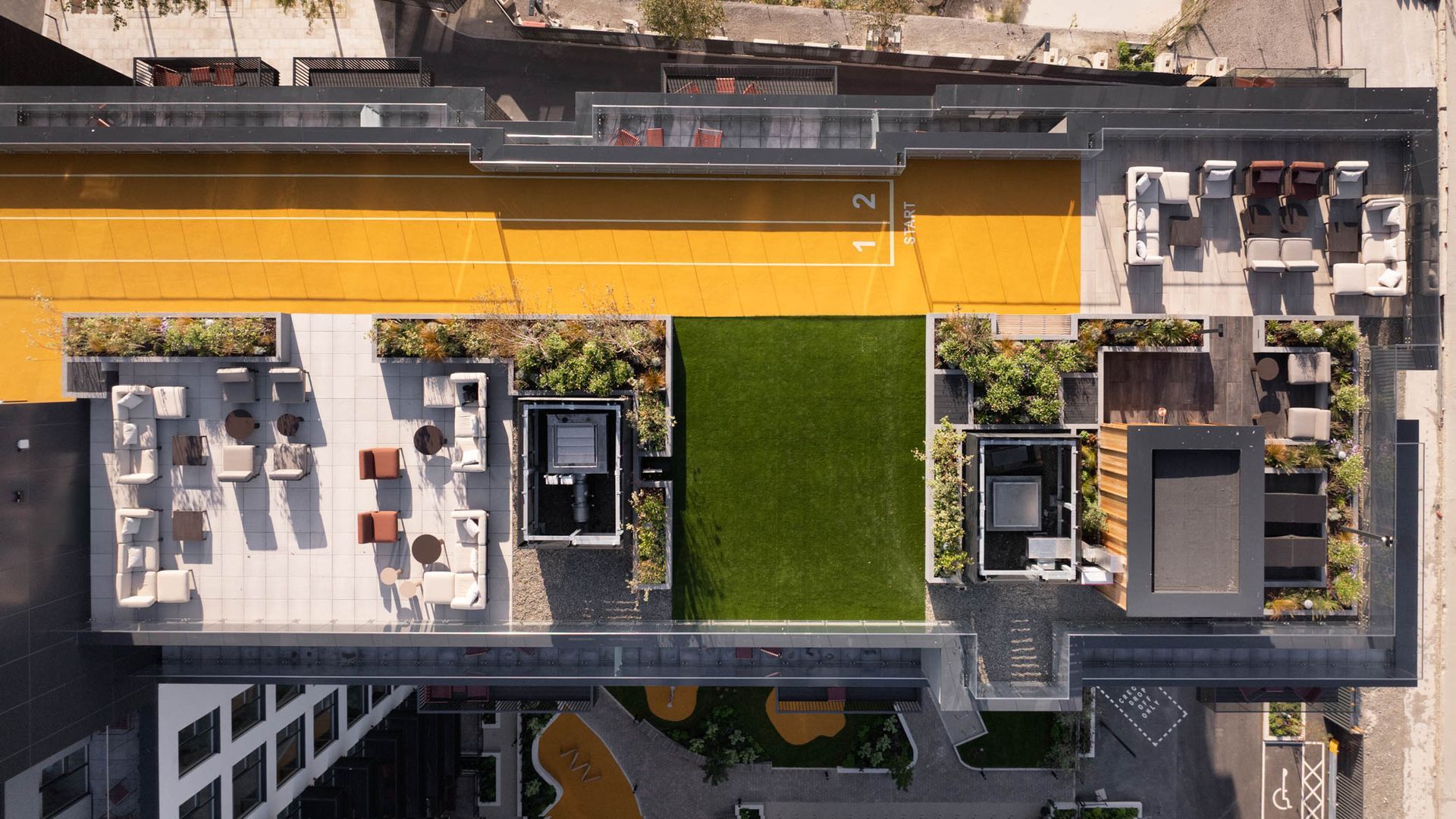Aerial view of a rooftop terrace with green lawn, seating areas, and a long yellow walkway along the building.
