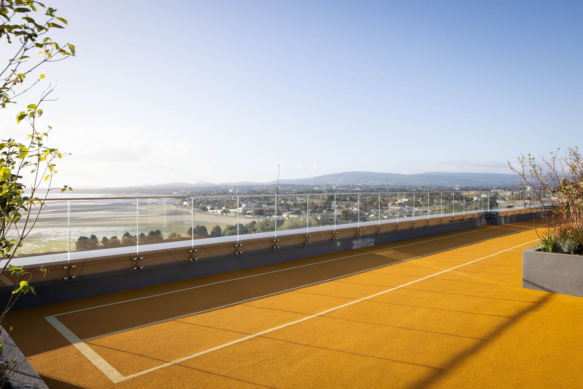 Rooftop terrace with orange flooring overlooking a distant cityscape and hills under a clear sky