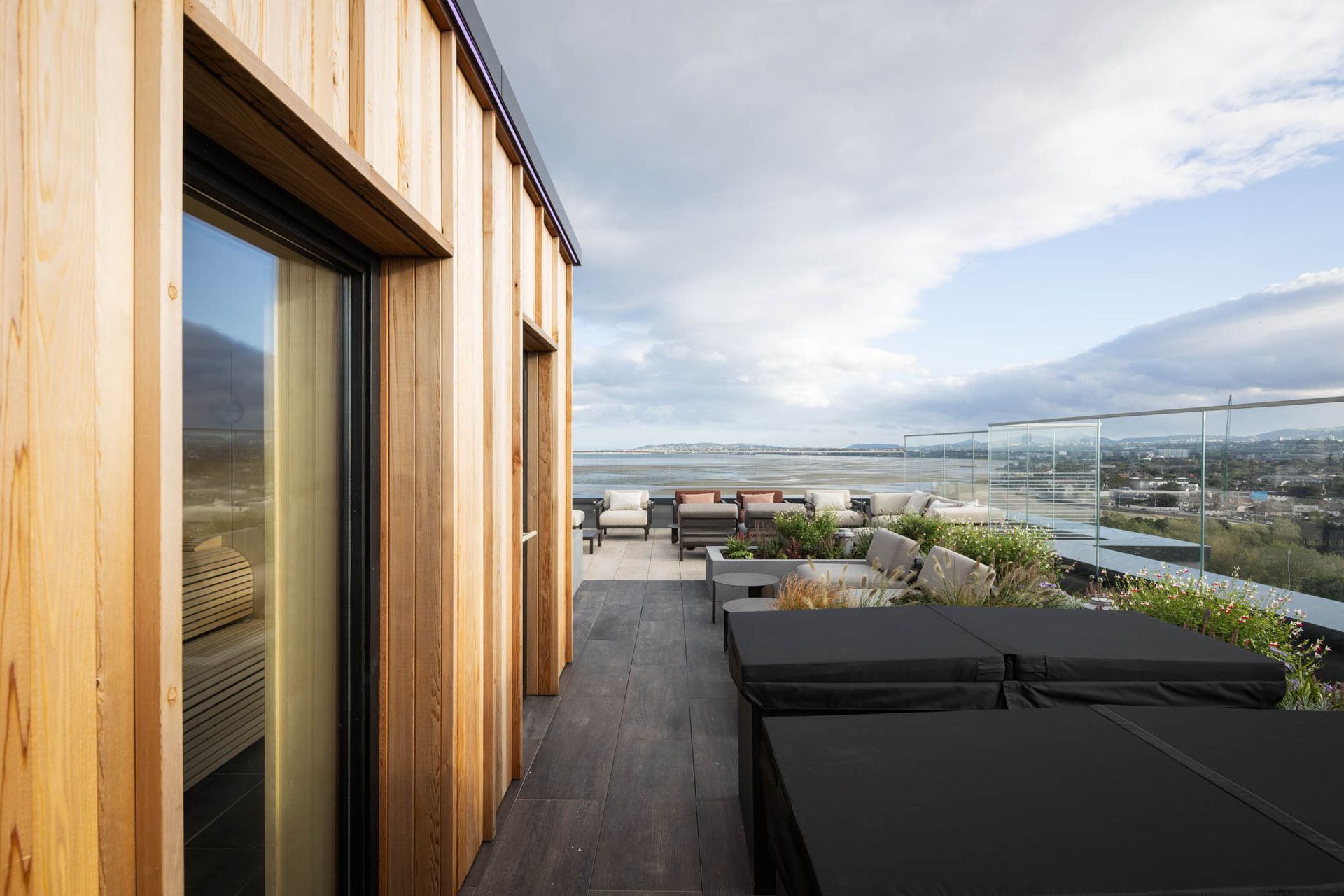Modern rooftop terrace with wooden siding, lounge chairs, and panoramic city and water view