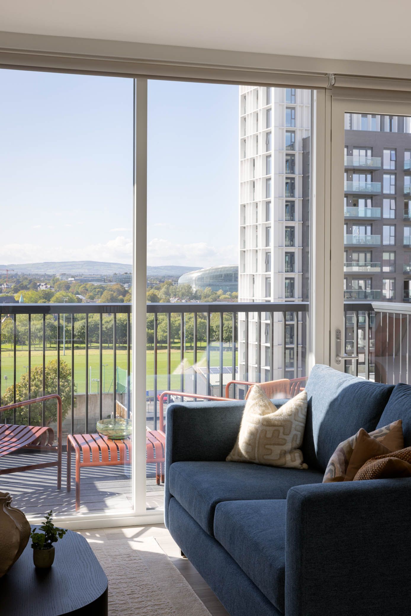 Sunlit living room balcony with blue sofa, cushions, and city view through sliding glass doors