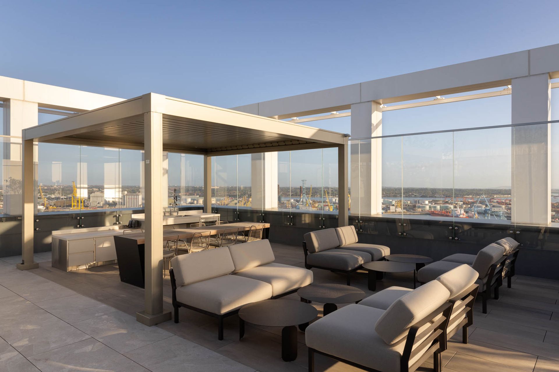 Rooftop lounge with beige sofas and pergola seating overlooking a city skyline at sunset