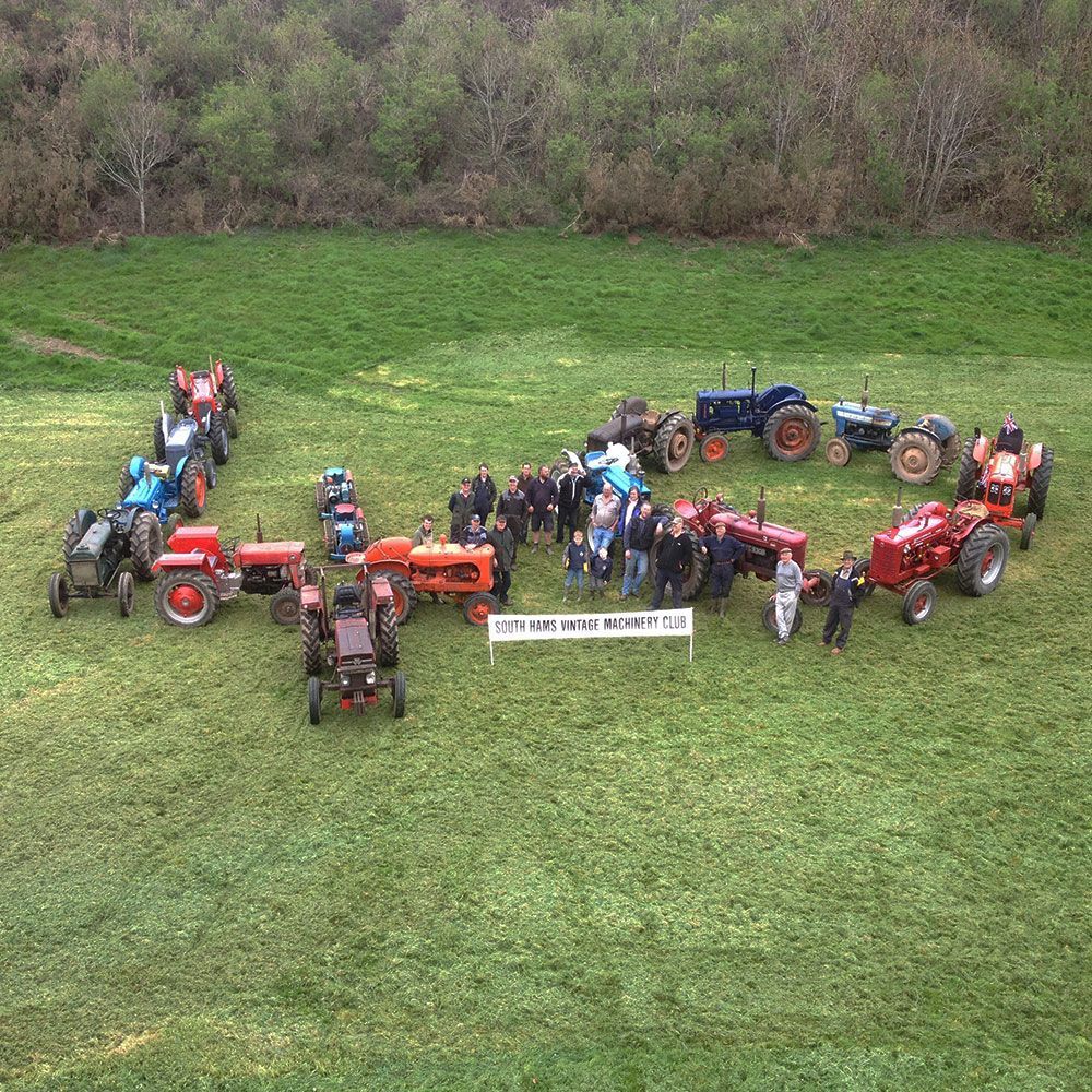 A group of people are standing in a field with tractors in the shape of the letter u.