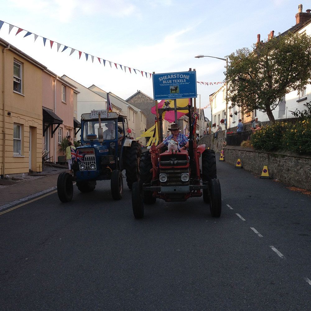 Two tractors are driving down a street and one has a sign that says wellington on it