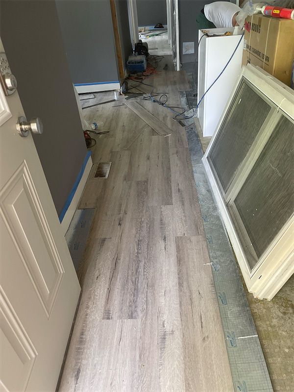 Hallway with new wood-look flooring being installed; white door on the left, window frame on the right.