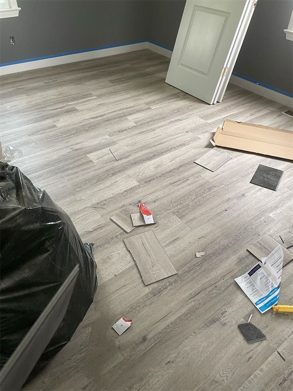 Room with gray wood-look flooring being installed. Cardboard, tools, and a door are present.