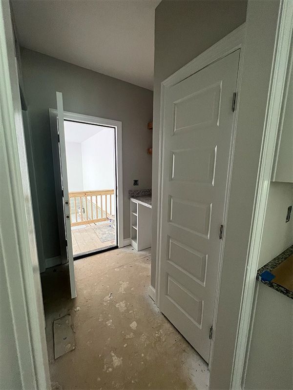 Interior view of a room with a white door, open door to a balcony, and unfinished floors.