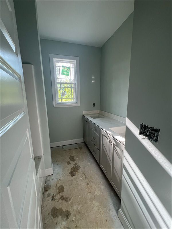 Bathroom under construction with gray cabinets, light green walls, and a small window.