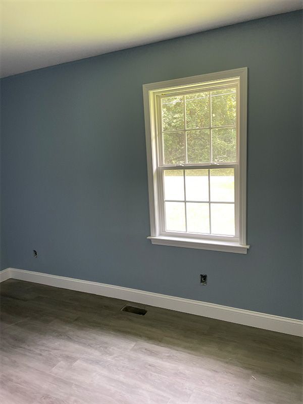 Blue-painted room with white trim, a window, and gray flooring.