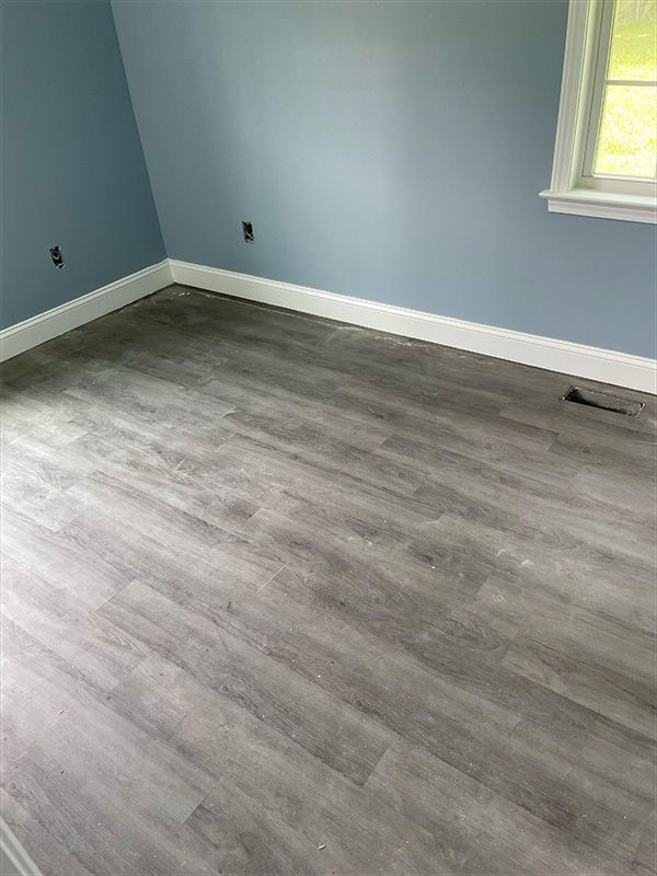 Room with gray wood-look flooring, blue walls, white trim, and a window.
