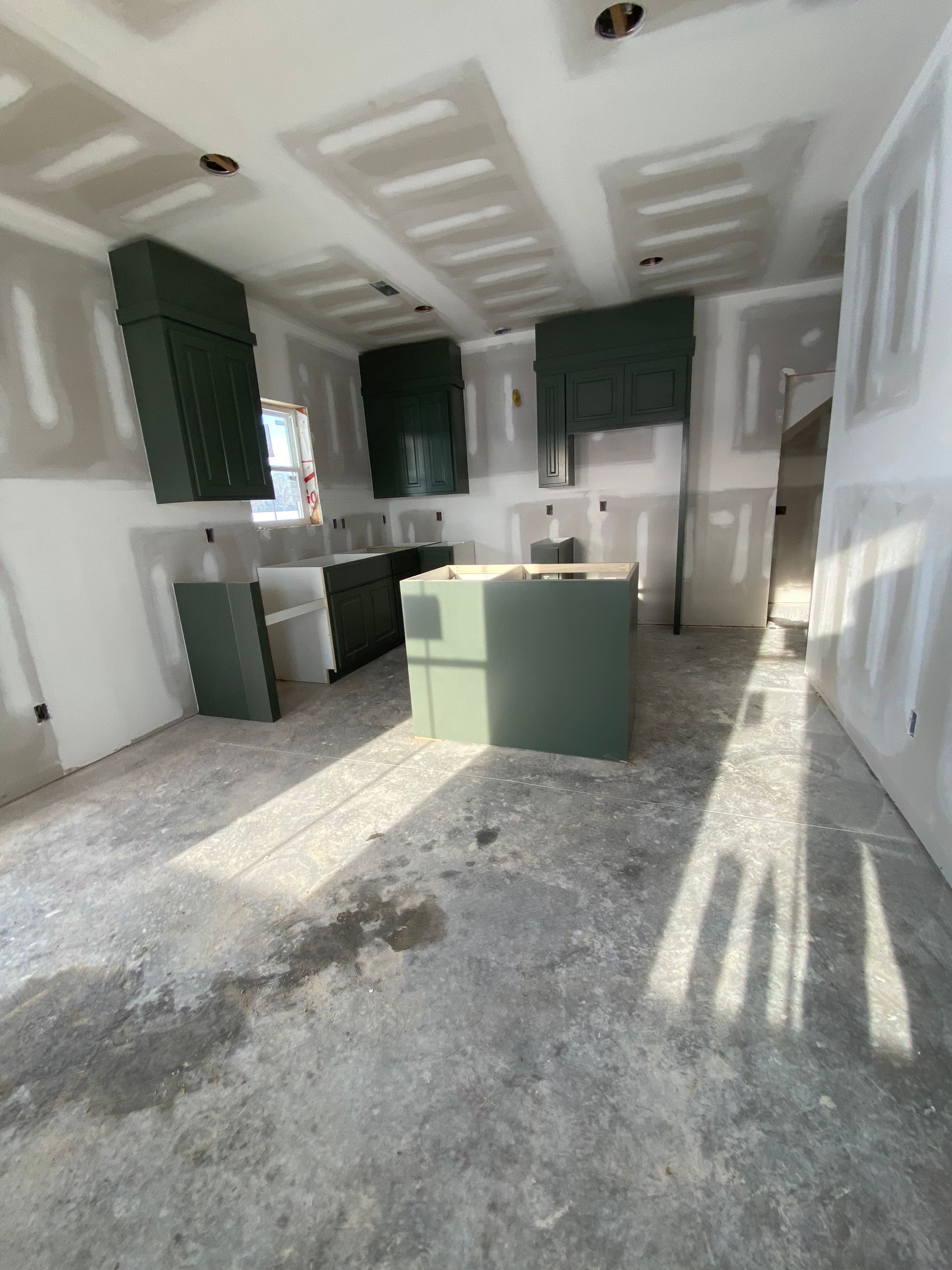 Unfinished kitchen interior with green cabinets, white walls, and sunlight casting shadows on the floor